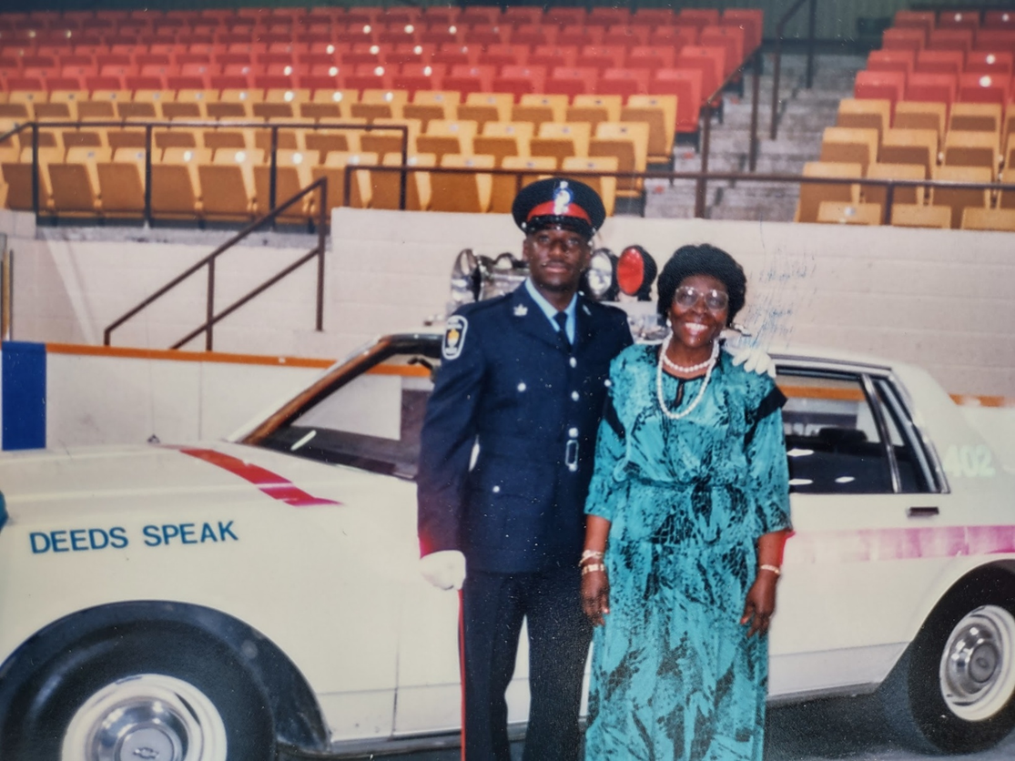 Cadet Keith Merith in dress uniform with his mother, beside a 'Deeds Speak' patrol car